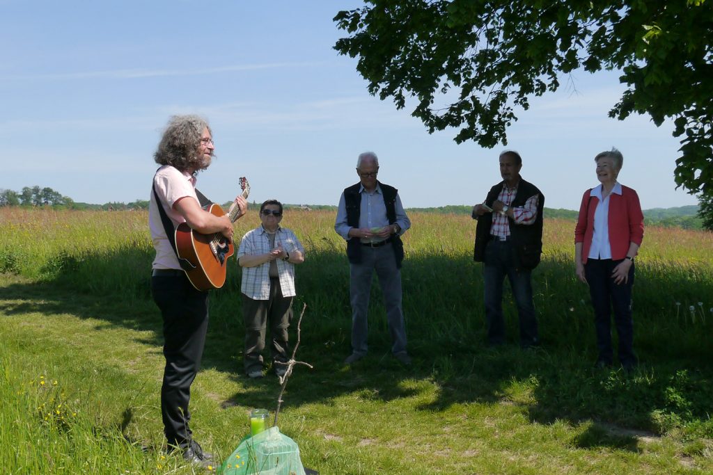 Ein Mann spielt Gitarre, mehrere andere Personen stehen um ihn herum und lächeln.
