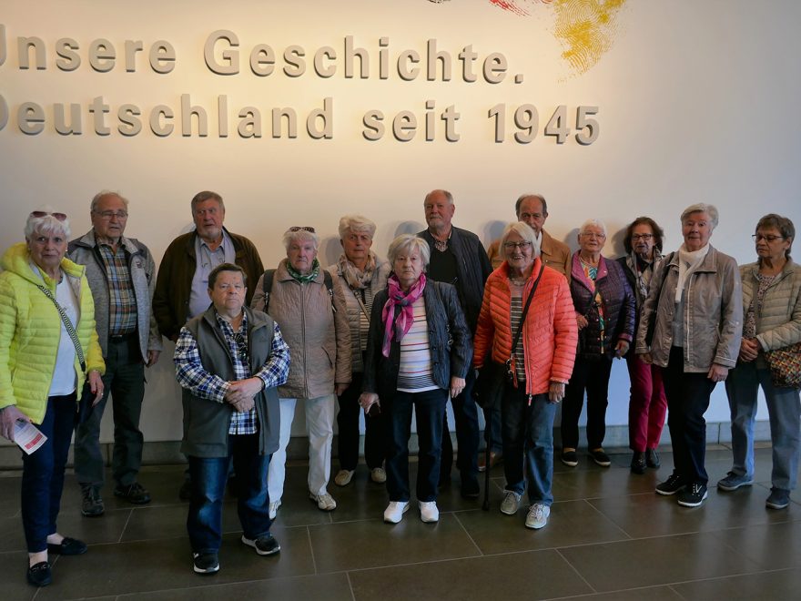 Teilnehmer der Tour posieren vor einer Wandbeschriftung im Haus der Geschichte in Bonn die lautet "Unsere Geschichte. Deutschland seit 1945"