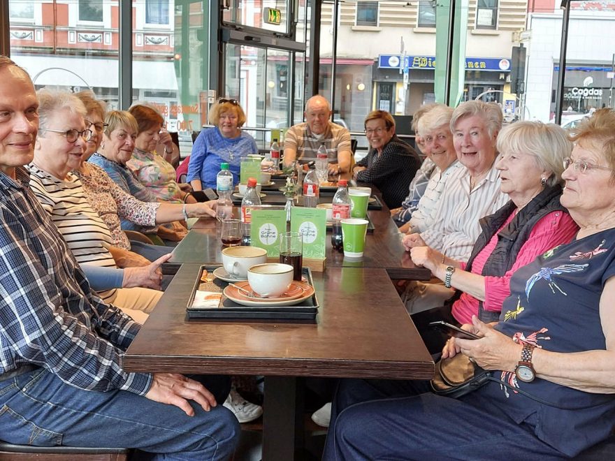 Mehrere Personen sitzen um einen Café-Tisch herum und plaudern.